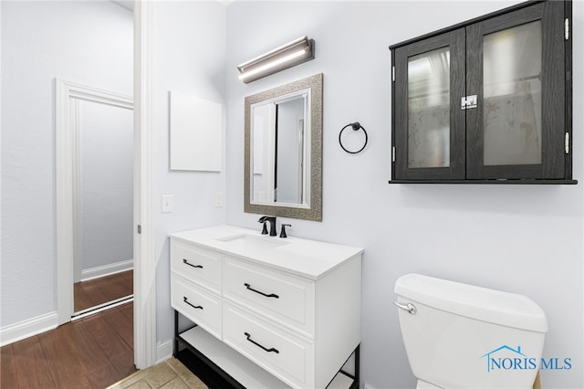 half bath featuring baseboards, wood finished floors, toilet, and vanity