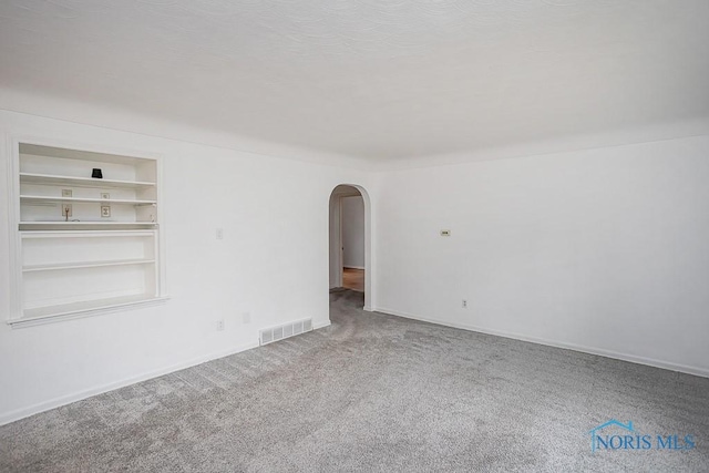 unfurnished room featuring visible vents, built in shelves, arched walkways, carpet, and baseboards