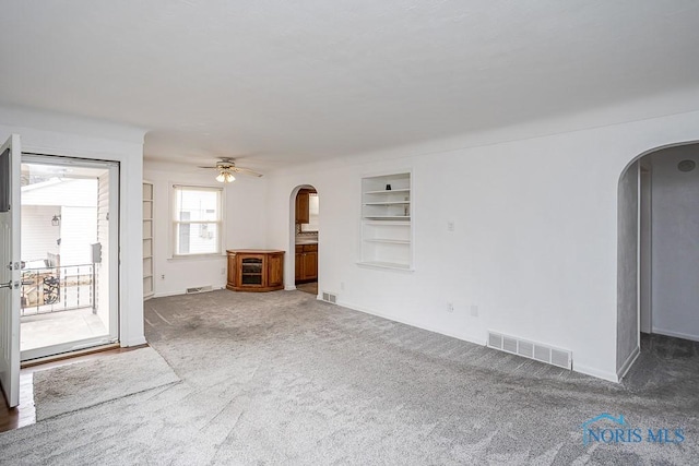 unfurnished living room featuring built in shelves, arched walkways, visible vents, and carpet floors