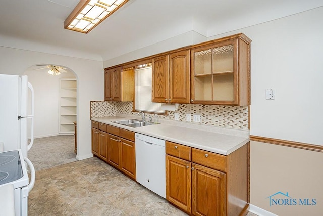 kitchen with brown cabinetry, light countertops, arched walkways, white appliances, and a sink