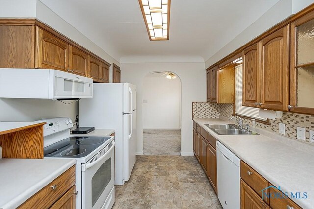 kitchen featuring tasteful backsplash, brown cabinetry, arched walkways, white appliances, and a sink