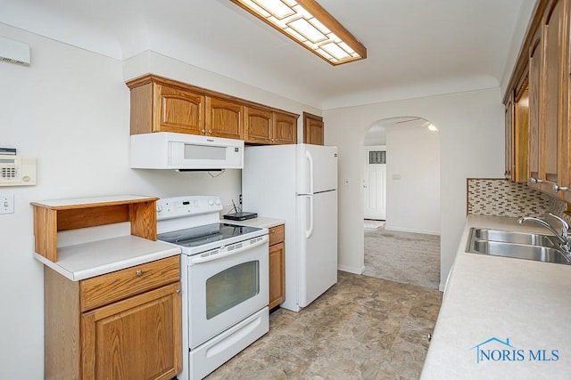 kitchen with a sink, white appliances, arched walkways, brown cabinetry, and light countertops