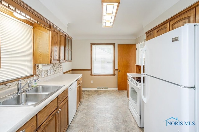 kitchen featuring visible vents, brown cabinets, white appliances, and a sink