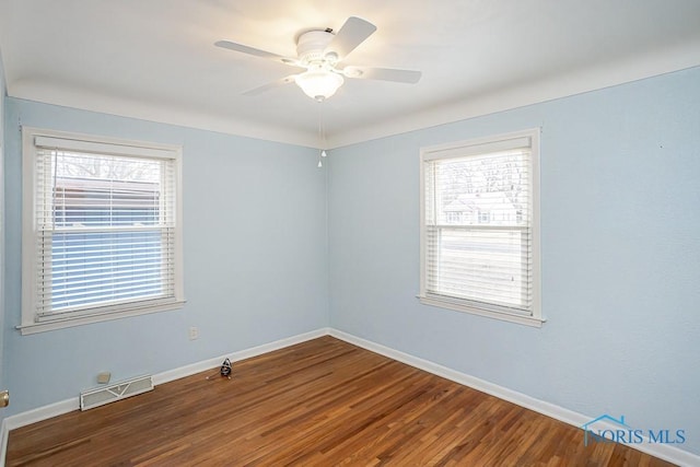 spare room featuring wood finished floors, visible vents, a wealth of natural light, and baseboards