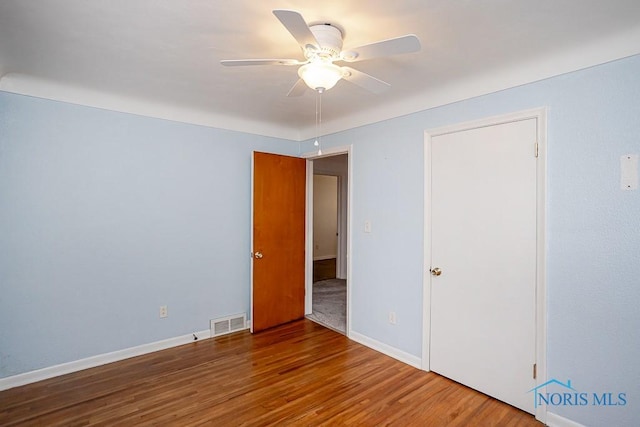 unfurnished room with a ceiling fan, wood finished floors, visible vents, and baseboards