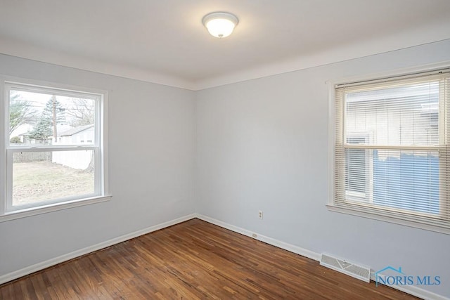 empty room featuring dark wood-style floors, visible vents, and baseboards