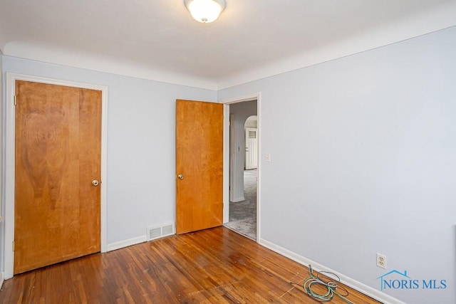 unfurnished bedroom featuring wood finished floors, arched walkways, visible vents, and baseboards