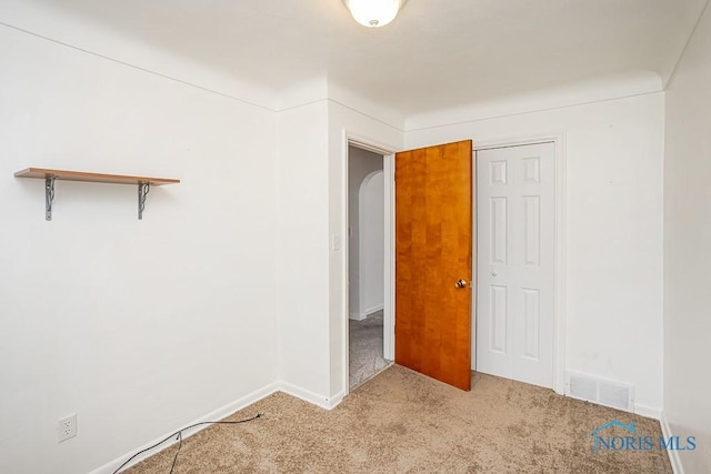 unfurnished room with visible vents, arched walkways, carpet floors, and baseboards