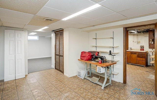 basement with a drop ceiling, visible vents, baseboards, and light floors