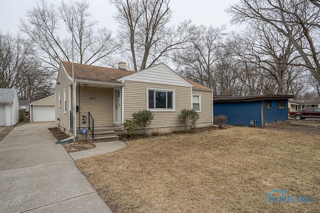 bungalow-style home featuring a detached garage, an outdoor structure, a chimney, and a shingled roof