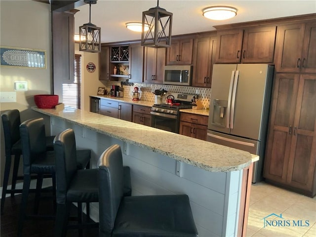 kitchen with a kitchen breakfast bar, stainless steel appliances, decorative backsplash, light stone countertops, and hanging light fixtures