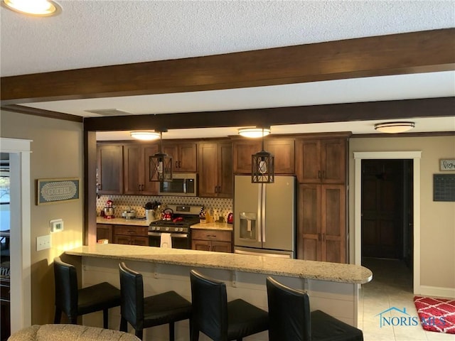 kitchen with stainless steel appliances, a kitchen bar, beam ceiling, hanging light fixtures, and a peninsula