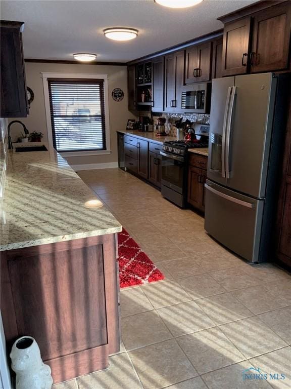 kitchen with stainless steel appliances, a sink, light stone countertops, and dark brown cabinetry