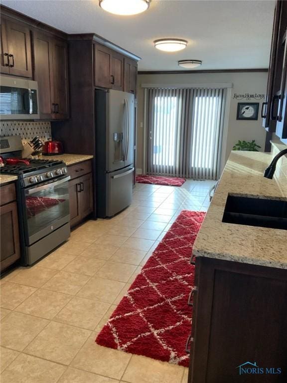 kitchen featuring a sink, stainless steel appliances, light tile patterned flooring, decorative backsplash, and dark brown cabinets