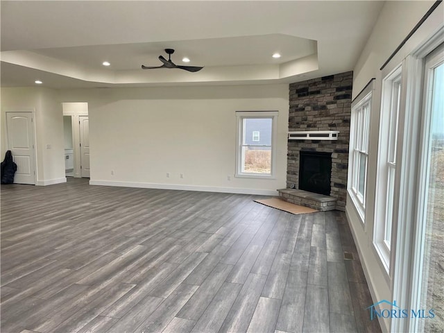 unfurnished living room with baseboards, a stone fireplace, recessed lighting, a raised ceiling, and dark wood-style flooring