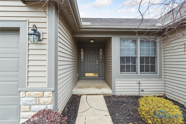 view of exterior entry featuring stone siding, an attached garage, and roof with shingles