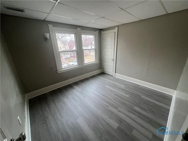 empty room featuring wood finished floors, a paneled ceiling, visible vents, and baseboards