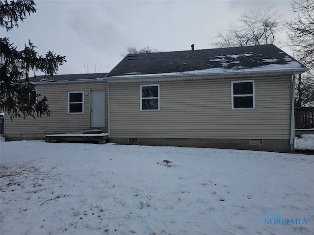 snow covered back of property with crawl space and roof with shingles