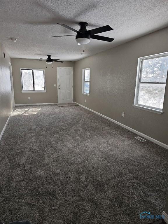 carpeted spare room featuring a textured ceiling, baseboards, ceiling fan, and visible vents