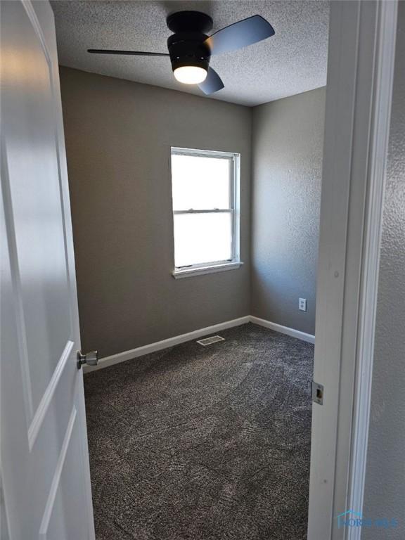 spare room featuring dark colored carpet, visible vents, baseboards, and a textured ceiling