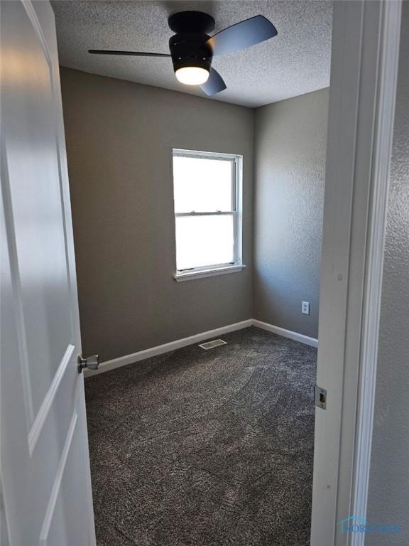 unfurnished room with baseboards, ceiling fan, dark carpet, and a textured ceiling