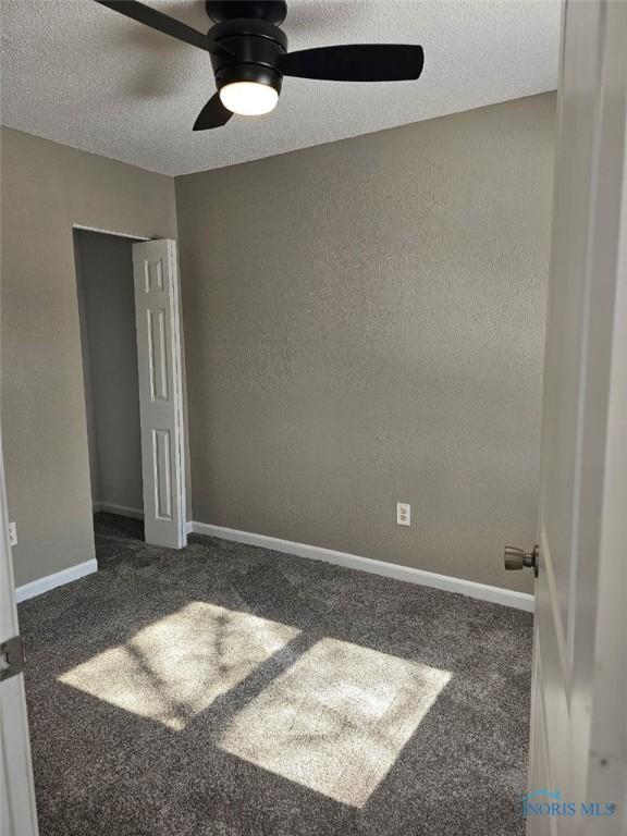 unfurnished room with baseboards, a ceiling fan, a textured wall, and a textured ceiling