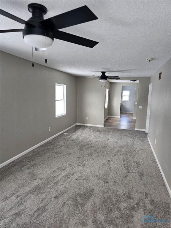 carpeted spare room featuring baseboards, a textured ceiling, and a ceiling fan