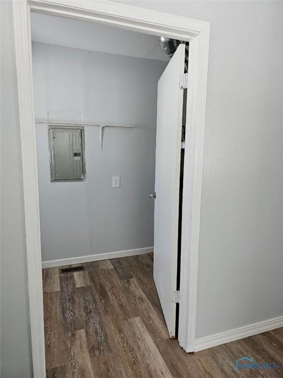 laundry room with electric panel, baseboards, and wood finished floors