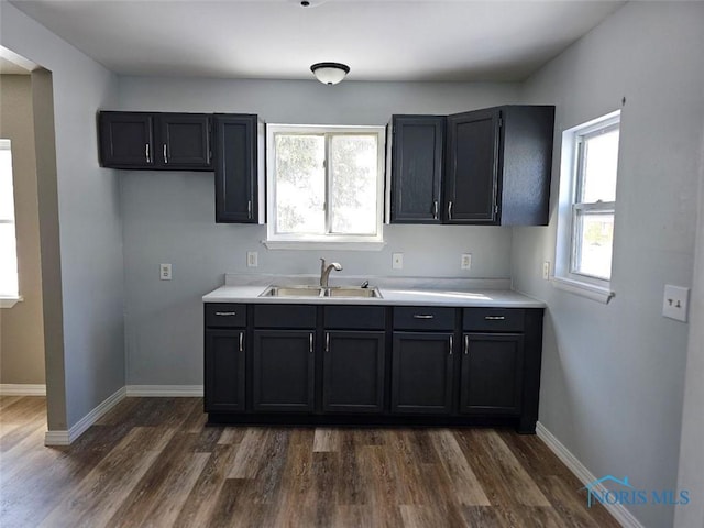 kitchen with light countertops, a sink, dark wood-style floors, and baseboards