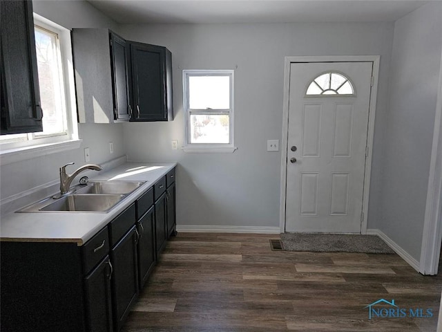 kitchen featuring a sink, baseboards, dark cabinets, light countertops, and dark wood-style flooring