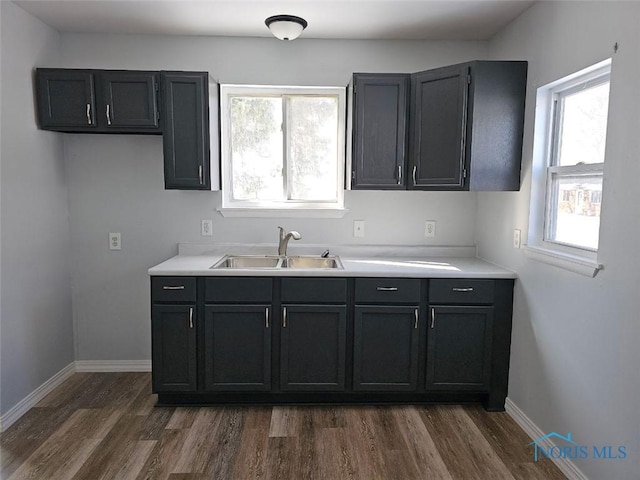 kitchen with a sink, baseboards, dark wood-type flooring, and light countertops