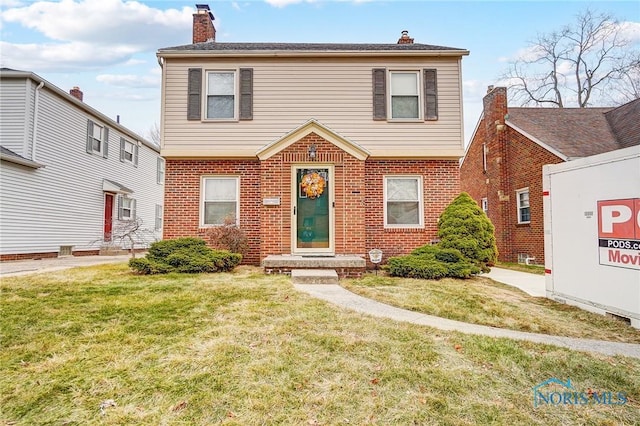 colonial home featuring a front yard, brick siding, and a chimney