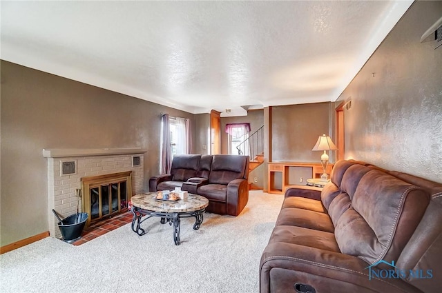 living room with a brick fireplace, stairs, a textured wall, and carpet floors