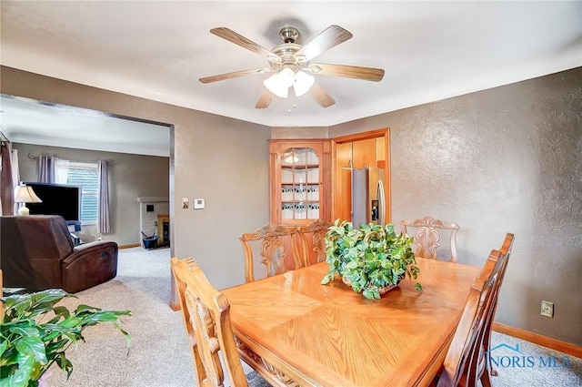 dining area featuring baseboards, light colored carpet, ceiling fan, and a textured wall