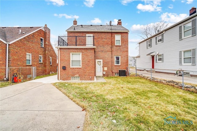 rear view of property featuring brick siding, fence, a lawn, a chimney, and a balcony