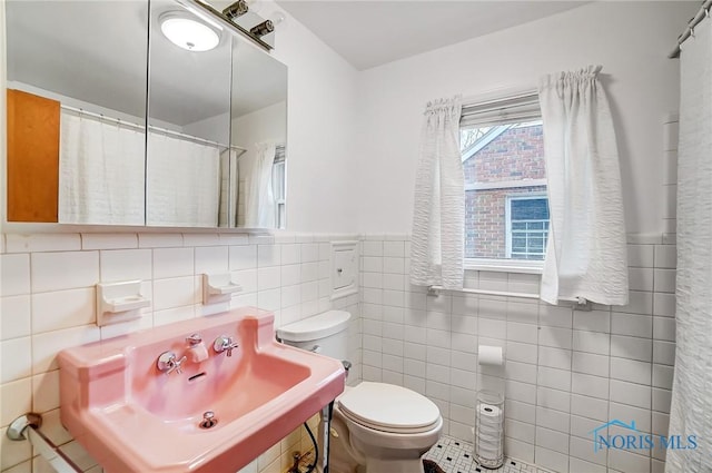 bathroom featuring toilet, a sink, curtained shower, tile walls, and wainscoting