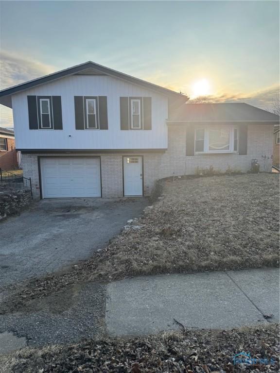 tri-level home featuring brick siding, an attached garage, and aphalt driveway