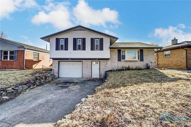 tri-level home featuring aphalt driveway, an attached garage, and brick siding