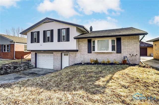 split level home featuring aphalt driveway, a garage, brick siding, and a chimney