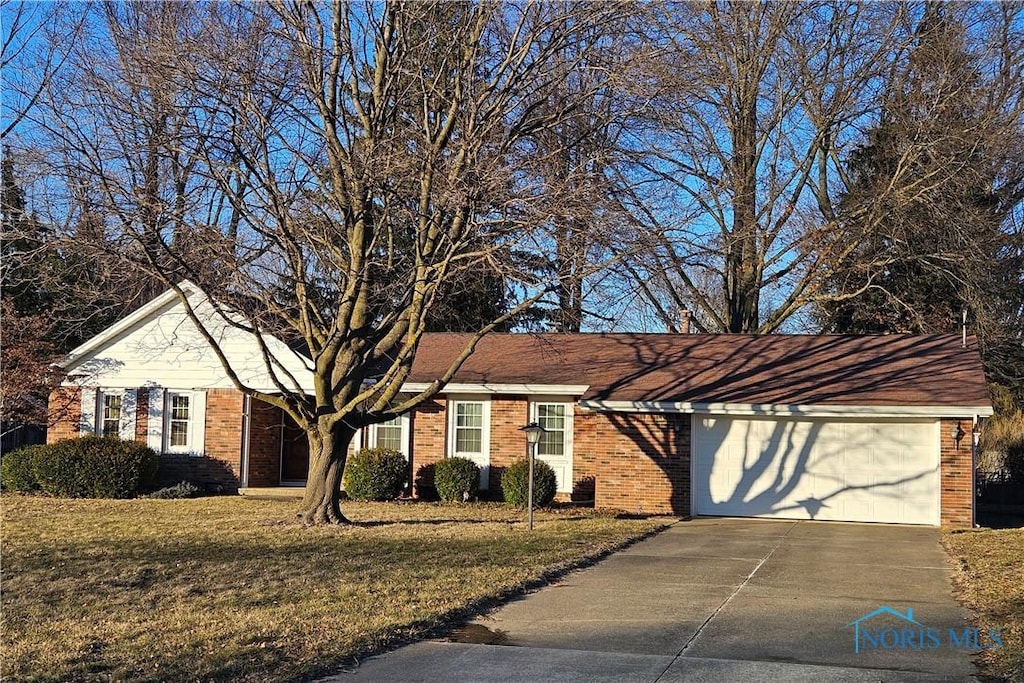 single story home with concrete driveway, a garage, brick siding, and a front lawn