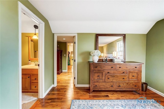 bedroom featuring baseboards, lofted ceiling, ensuite bathroom, wood finished floors, and a sink