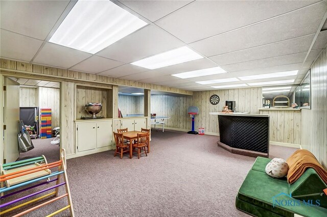 game room with a drop ceiling, carpet floors, wooden walls, a bar, and baseboards