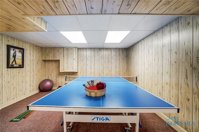 recreation room featuring wooden walls, a paneled ceiling, baseboards, and carpet floors