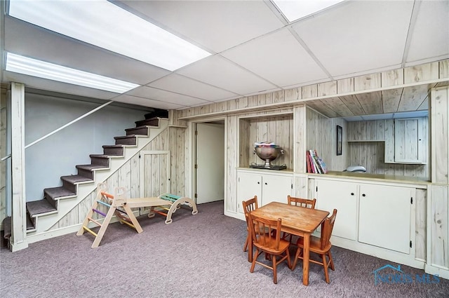 carpeted dining room with stairway, wood walls, and a drop ceiling