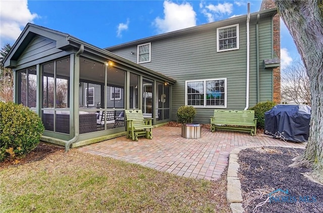 rear view of property featuring a chimney, a patio, and a sunroom