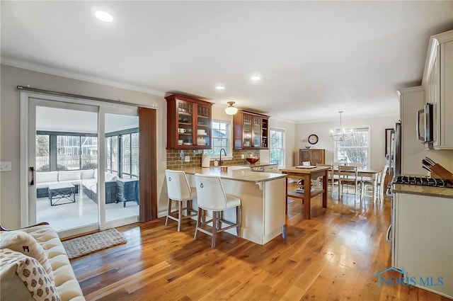 kitchen with a breakfast bar, ornamental molding, stainless steel microwave, tasteful backsplash, and light wood finished floors