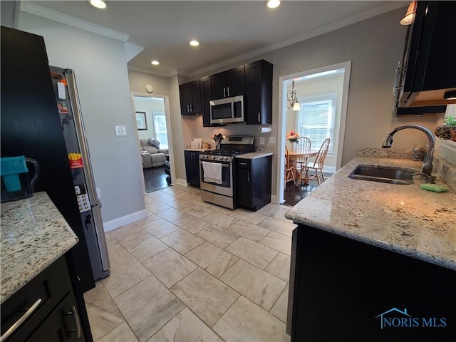 kitchen with dark cabinetry, light stone countertops, a sink, stainless steel appliances, and crown molding