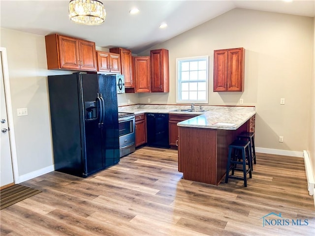 kitchen featuring a peninsula, a sink, black appliances, light countertops, and a kitchen breakfast bar