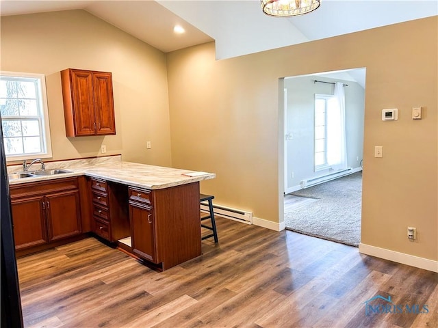 kitchen with vaulted ceiling, a baseboard radiator, a peninsula, and a sink