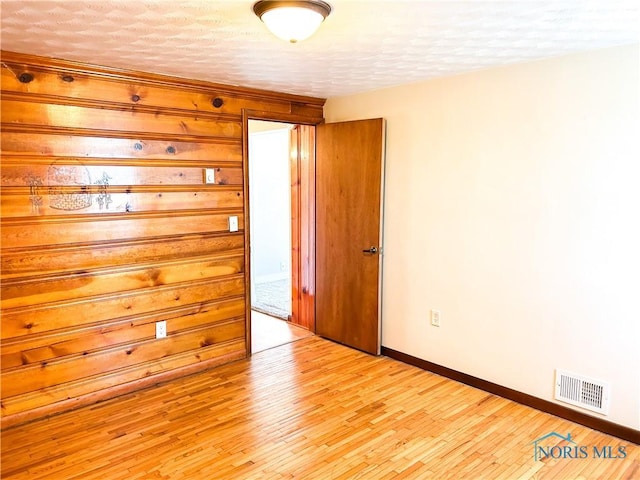 unfurnished room with light wood finished floors, visible vents, a textured ceiling, and baseboards